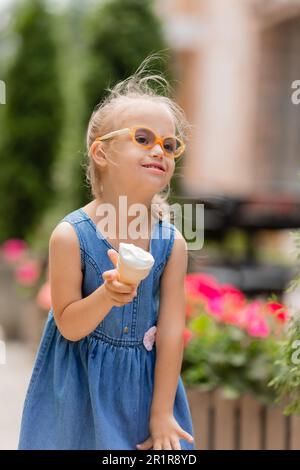 una ragazza un po 'felice con la sindrome di down mangia gelato in estate su una passeggiata Foto Stock