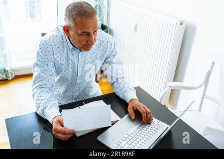 l'uomo fa i calcoli, guarda attraverso il rapporto finanziario del registratore di cassa domestico Foto Stock