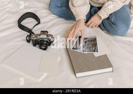 Donna seduta su un letto con una fotocamera digitale che guarda le foto stampate Foto Stock