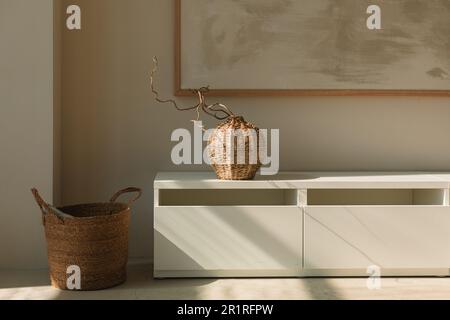 Vaso in vimini su un fianco sotto una cornice e cesto in un soggiorno Foto Stock