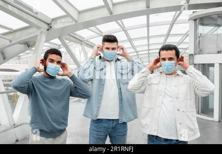 Tre ragazzi turisti che indossano maschere protettive mediche in aeroporto Foto Stock