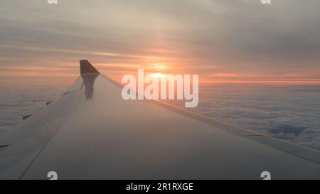 Ammira l'ala del jet Aircraft con il sole arancione all'orizzonte in volo sopra le nuvole Foto Stock