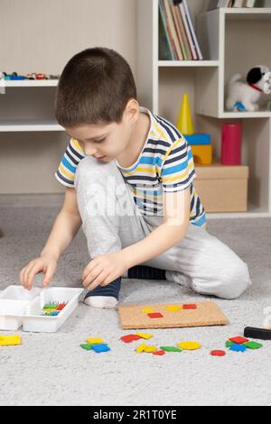 Un ragazzo di 5 anni crea un'immagine da pezzi multicolore di un mosaico su una lavagna. Foto Stock