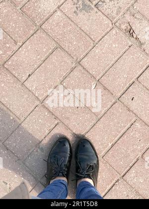 Vista dall'alto delle gambe, delle scarpe, dei piedi delle ragazze, delle donne in pelle verniciata sullo sfondo di una mattonella rettangolare in cemento rosso marrone. Foto Stock