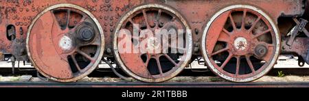 Ruote rosse arrugginite di una vecchia locomotiva a vapore obsoleta Foto Stock