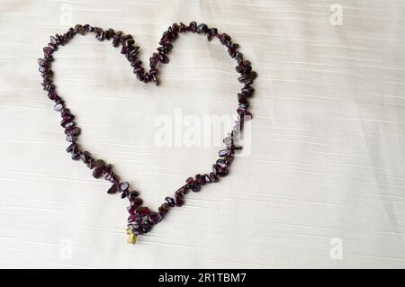 Cuore fatto di belle perle femminili, collane di pietre marrone scuro, ambra su uno sfondo di tessuto beige e spazio per il testo. Foto Stock
