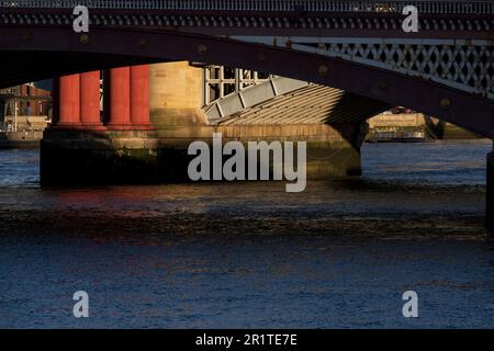 Una vista attraverso uno degli archi del ponte Blackfriars Road attraverso il Tamigi, di un pilastro illuminato dal sole del ponte della ferrovia Blackfrairs. Nero Foto Stock