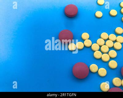 pillole colorate rosa, gialle volumetriche e rotonde di forma su sfondo blu opaco e di carta. farmaci per la salute. medicinali a base di erbe. backgroun medico Foto Stock