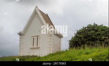 Una piccola casa bianca sulla cima di una collina erbosa Foto Stock