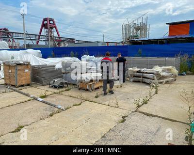 I lavoratori di sesso maschile attraversano un magazzino di attrezzature industriali e materiali in scatole in un'area di stoccaggio all'aperto. Vista dal retro. Foto Stock