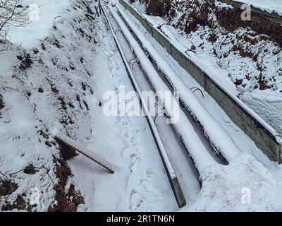 tubi lunghi, sottili, neri, stretti per la posa di impianti idraulici. i tubi in polipropilene sono ricoperti da uno strato di neve in una nuova zona residenziale. re Foto Stock