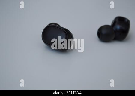 le piccole cuffie wireless nere si trovano su una superficie bianca. un dispositivo per ascoltare musica in un angolo macro. splendido accessorio elegante. comodi musi Foto Stock