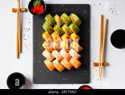 Set di involtini colorati con gamberi, salmone, avocado, formaggio, zenzero sottaceto, wasabi, salsa di soia, bastoncini cinesi su sfondo bianco, vista dall'alto. Foto Stock