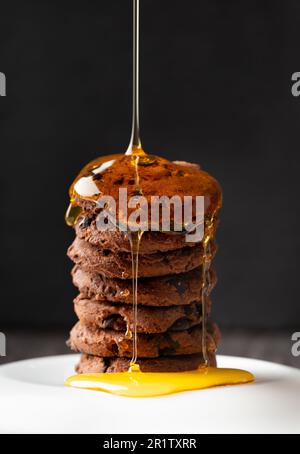 Il miele si versa su biscotti fatti in casa con scaglie di cioccolato in un primo piano su sfondo scuro. Composizione di biscotti artigianali con pezzetti di cioccolato e miele Foto Stock
