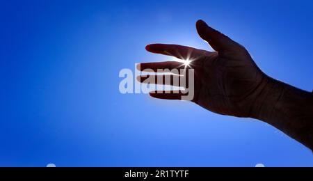 Mano che raggiunge il cielo in cerca di aiuto con sunstar ispirazione sunshine guida dall'alto Foto Stock