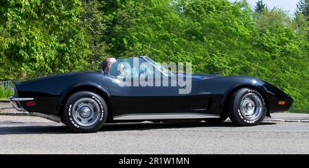 Stoke Goldington, Northants, Regno Unito - Maggio 14th 2023. 1973 nero CHEVROLET CORVETTE STINGRAY guida attraverso un villaggio inglese Foto Stock