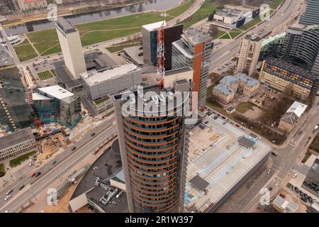 Fotografia in drone del tetto del grattacielo, dell'antenna su di esso e degli edifici di uffici circostanti. Vista ad angolo alto. Foto Stock