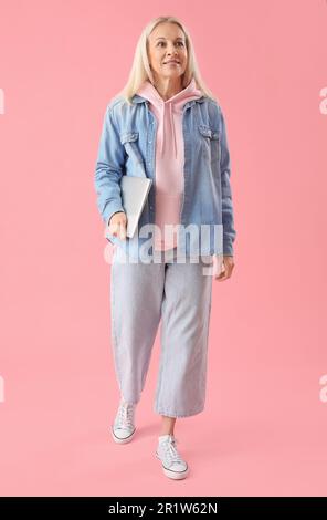 Programmatore femmina maturo con laptop su sfondo rosa Foto Stock