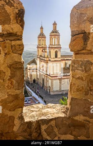 La chiesa di nostra Signora dell'Incarnazione vista attraverso i bastioni del Castello di Olvera nella città di Pueblo Blanco di Olvera, Spagna. La chiesa parrocchiale fu costruita nel 1822 ma il castello fu costruito dai governanti arabi nel 12th ° secolo su una fondazione lasciata dai Romani nel 3rd ° secolo. Foto Stock