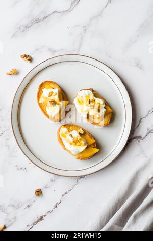 Fette di baguette con formaggio cremoso, persimmon, miele e noci su sfondo marmoreo. Bruschetta antipasti. Sapore dolce salato, ricetta gourmet antipasto Foto Stock