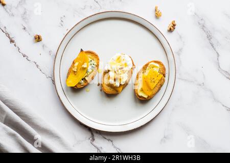 Fette di baguette con formaggio cremoso, persimmon, miele e noci su sfondo marmoreo. Bruschetta antipasti. Sapore dolce salato, ricetta gourmet antipasto Foto Stock