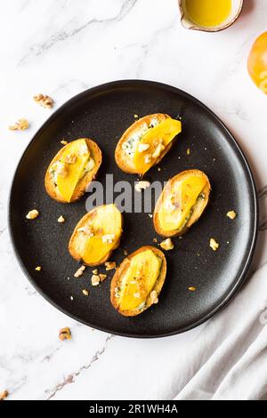 Fette di baguette con formaggio cremoso, persimmon, miele e noci su sfondo marmoreo. Bruschetta antipasti. Sapore dolce salato, ricetta gourmet antipasto Foto Stock