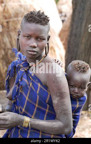 Valle di Omo, Etiopia â€“ 11.17.2022: Donna della tribù Mursi che porta il suo bambino Foto Stock