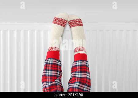 Bambina che scalda i piedi vicino al radiatore di riscaldamento interno, primo piano Foto Stock