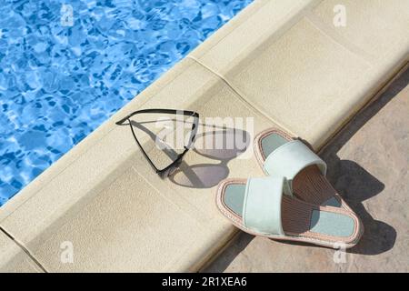 Occhiali da sole e ciabatte eleganti a bordo piscina nelle giornate di sole. Accessori da spiaggia Foto Stock