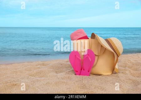 Borsa estiva con pantofole, telo da spiaggia e cappello di paglia sulla sabbia vicino al mare, spazio per testo Foto Stock