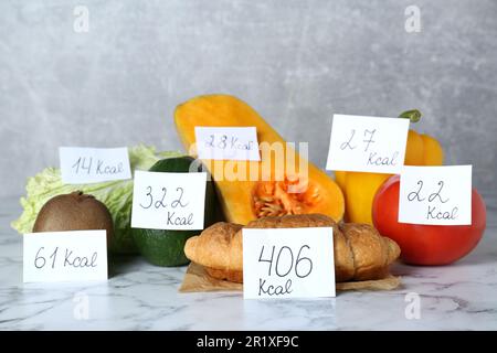 Prodotti alimentari con etichette di potere calorifico su tavola in marmo bianco. Concetto di perdita del peso Foto Stock