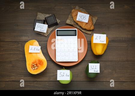 Calcolatrice e prodotti alimentari con etichette di potere calorifico su tavola di legno, piano di posa. Concetto di perdita del peso Foto Stock