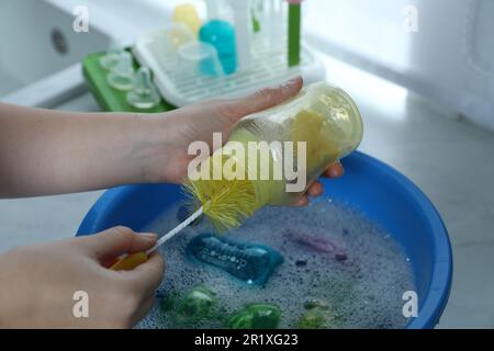 Donna lavaggio biberon sopra il bacino in cucina, primo piano Foto Stock