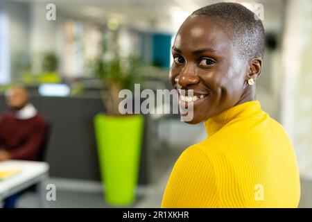 Ritratto di sorridente afroamericana businesswoman con capelli corti guardando oltre la spalla in ufficio Foto Stock