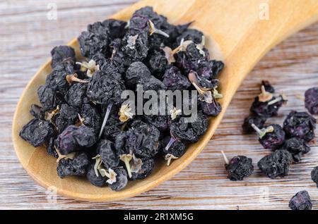 Frutti di bosco neri o frutti di goji neri, in un cucchiaio di legno sul tavolo. Erbe cinesi comunemente usate nella medicina cinese tradizionale. Foto Stock