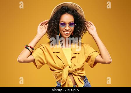 Divertente donna turistica dai capelli ricci che indossa un cappello di paglia sorridente e molto felice durante le vacanze. Viaggiatrice afroamericana Foto Stock