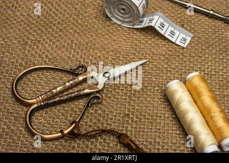 Alcuni pezzi da cucire a casa con rocche di fili tan, forbici in rame vintage su tela di tela con metro a nastro bianco Foto Stock