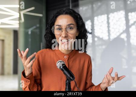 Webcam vista, pov successo ispanica donna parlare videochiamata con gli amici che lavorano in ufficio sul posto di lavoro, donna d'affari con microfono professionale registrazione corso di formazione business Foto Stock