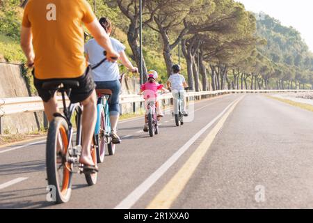 Famiglia di quattro persone, genitori con figlio e figlia si rilassano in bicicletta su un percorso costiero, con una vista sul mare Foto Stock