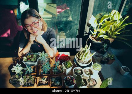 donna e pianta succulenta nella pentola che pianta seduta al tavolo di lavoro della serra Foto Stock