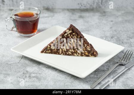 Torta al mosaico al cioccolato con noci su un piatto di porcellana bianca su fondo in pietra Foto Stock