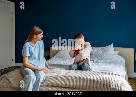 Grata piccola scatola del regalo del abbraccio del figlio si siede sul letto. Mamma amorevole e premurosa che saluta il bambino con il compleanno Foto Stock