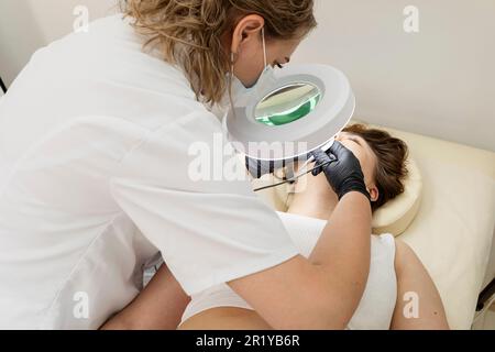 Dermatologo Rimozione dei capelli sul mento del viso del paziente con procedura di elettrolisi, epilazione elettrica nel salone di bellezza. Trattamento di rimozione dei capelli Foto Stock