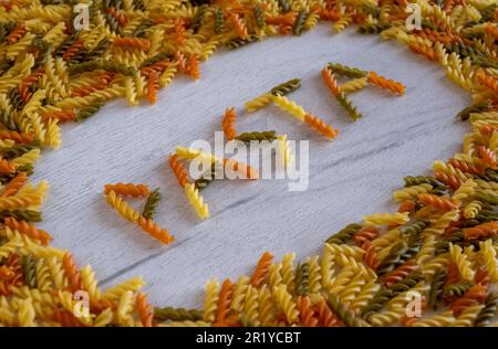 La parola pasta è costituita da fusilli su fondo di legno bianco su cornice di pasta Foto Stock