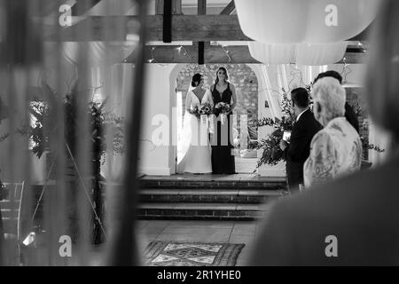 Giorno di nozze, sposa che collega le braccia con la sorella mentre camminavano lungo la navata il suo giorno di nozze, sposa / sorella sta guardando attraverso la sua Maid of Honor Foto Stock