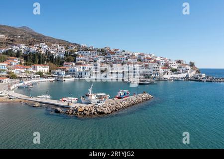 Andros isola, Batsi villaggio, Cicladi destinazione Grecia. Vista del tradizionale edificio imbiancato di bianco, del porto, della barca ormeggiata, del cielo blu chiaro dell'acqua di mare. Foto Stock