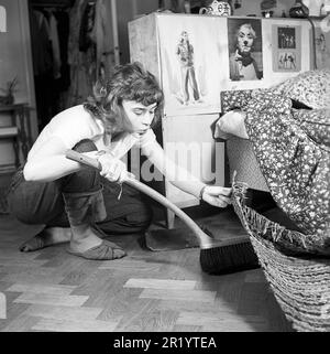 Giorno di pulizia nel 1950s. Un interno di una giovane donna che pulisce il floor.She solleva il tappeto e nasconde lo sporco sotto di esso per più tardi. L'espressione di spazzare qualcosa sotto il tappeto è talvolta utilizzata quando si descrive per nascondere qualcosa o nascondere un problema di embarresing, per coprire. È attrice svedese Harriet Andersson. Svezia 1951. Rif. Conard 1608 Foto Stock