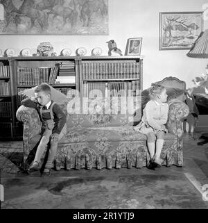 Negli anni '1950s. Due bambini sono seduti alle estremità del divano, visibilmente arrabbiati e sconvolti l'uno con l'altro, non disposti a fare amicizia. Rif. Conard 1716 Foto Stock