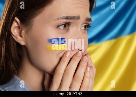 Triste giovane donna con mani attaccate vicino alla bandiera Ucraina, primo piano Foto Stock