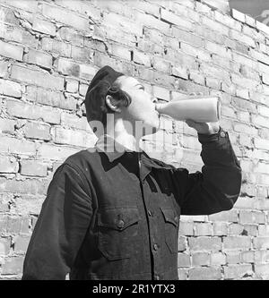 Negli anni '1950s. Una giovane apprendista di mattoni beve da una bottiglia di latte al sole durante una pausa al lavoro. Sullo sfondo si vede un muro di mattoni di nuova costruzione. A questo punto il latte è stato venduto e consegnato in bottiglie di vetro o si potrebbe comprare il latte per portare a casa dal negozio nel proprio biberon. Svezia 1951. Kristoffersson rif BB94-11 Foto Stock